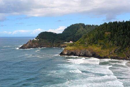 rich beautiful scenic view of the oregon coast with waves crashing and lighthouse off in the distanceの写真素材