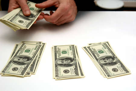 man counting out hunderd dollar bills in three stacks on white table