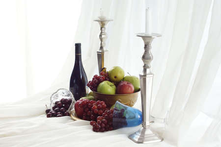 Candlesticks, red wine and brass fruit bowl overflowing onto table