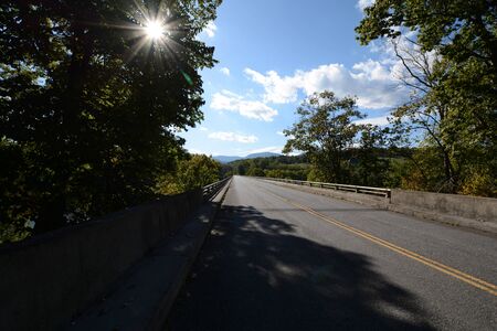 Road leading to bridge with starburst sun and shadowsの写真素材
