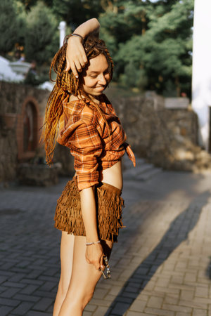 a girl with a dreadlocked hairstyle poses in summer outdoor, bright sunlight, dressed in a plaid shirt and shortsの写真素材