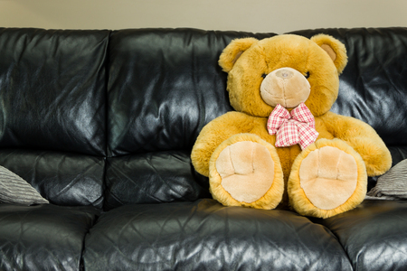 Big brown teddy bear sitting in black sofaの写真素材