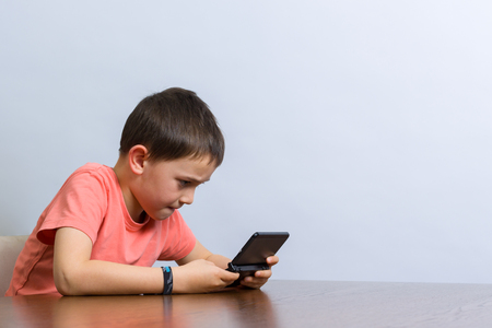 Young boy playing handheld video game at a table. Against grey backgroundの写真素材