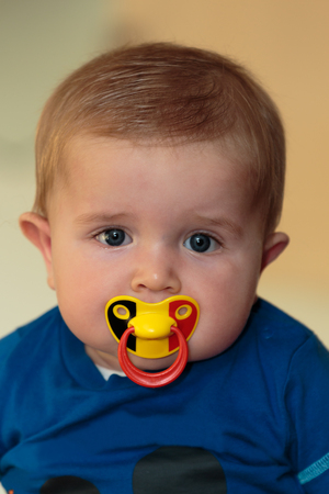 Cute baby boy (6 months old) with belgian tricolore (black, yellow, red) pacifierの写真素材