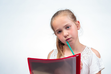 A cute 10-year-old caucasian schoolgirl looking a bit worried while holding a pencil against her chinの写真素材