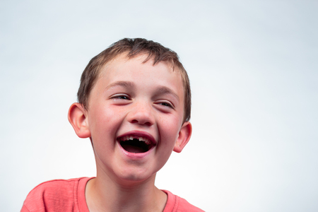 Close up portrait of a caucasian 8 year old boy laughing with open mouth, milk tooth missing. isolated on light backgroundの写真素材