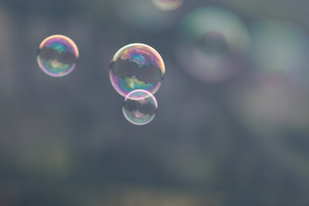 Three soap bubbles flying through the air on a blurry dark gray backgroundの写真素材