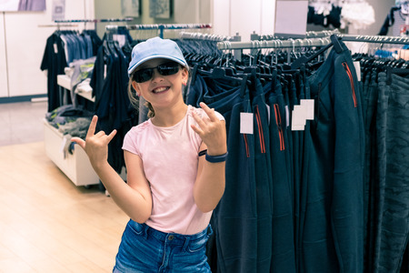 Portrait of young trendy girl with pink t-shirt, sunglasses and baseball cap in department store