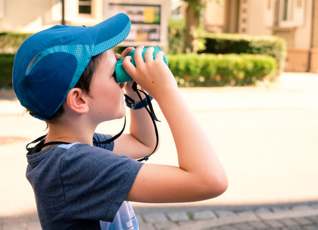 8 year old boy with blue baseball hat looking through toy binocularsの写真素材