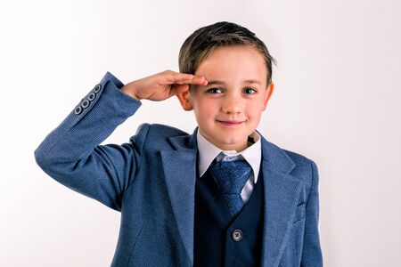 close-up portrait of 8 year old boy dressed in a suit salutingの写真素材