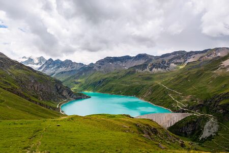View on the reservoir Lac de Moiry and the concrete dam surrounded by green alpine pastures high up in the Pennine Alps on cloudy day in summer. Grimentz, Valais, Switzerland, Europeの写真素材