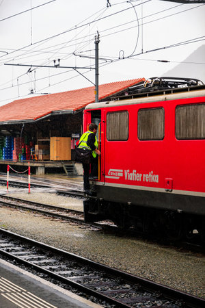 Pontresina, Grisons, Switzerland - August 9 2016 : Train driver wearing yellow safety vest enters his red locomotive from the Rhaetian Railway (RhB) in the railway station of Pontresina on a rainy dayのeditorial素材