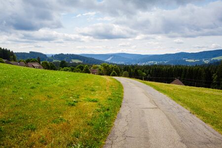 picturesque panorama with deserted road between sloping meadows in the High Black Forest landscape in Breitnau, Baden-WÃ¼rttemberg, Germany on a cloudy day in summerの写真素材