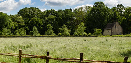 Wide panorama of rural Flemish landscape of pasture with wooden fence an old brick house and a treeline in the background some white cloudsの写真素材