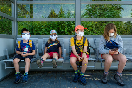 Aha, Baden-WÃ¼rttemberg, Germany - July 28 2020: 4 children (between 5 and 12 years old), sitting on a bench waiting for a train, wearing face masks. corona virus prevention measuresのeditorial素材