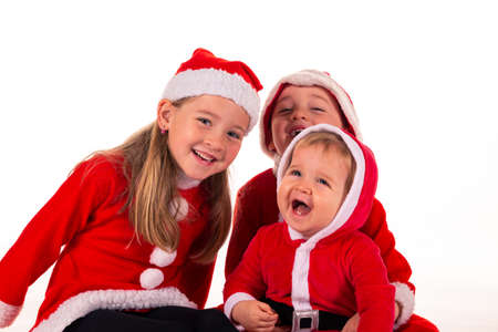 3 children, 2 boys (1 year old - 4 year old) 1 girl (6 years old) sitting together on the floor in Santa Claus costume laughing. isolated on whiteの写真素材
