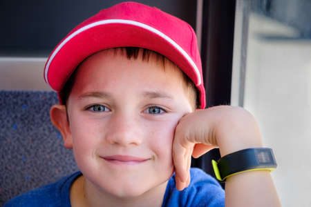 close up portrait of a 9 year old boy wearing a red baseball hat holding his hand to his faceの写真素材