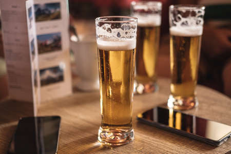 A wooden table in a pub or bar with 3 glasses of gold colored foamy beer and 2 mobile phones. no visible peopleの写真素材