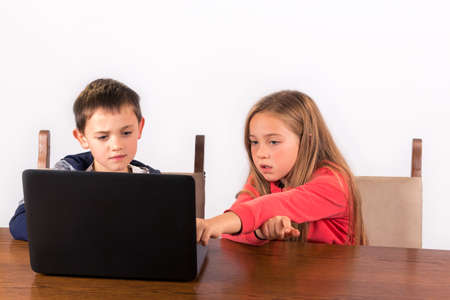 Young girl and boy - brother and sister - working on a laptop, girl pointing at screen. isolated on white backgroundの写真素材