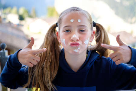 Cheerful young caucasian girl with ponytail points to her face while applying sunblock cream. sun protection conceptの写真素材