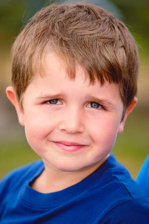 close up headshot portrait of cheerful 7 year old caucasian boy smiling with mouth closed looking at camera. outdoors shallow depth of fieldの写真素材