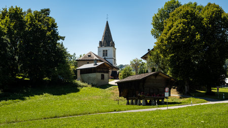 Picturesque alpine summer landscape view with small white church, wooden buildings, trees and green pastures - Cergnat, Ormont-Dessous near Aigle in Swiss canton of Vaud, Switzerlandの写真素材