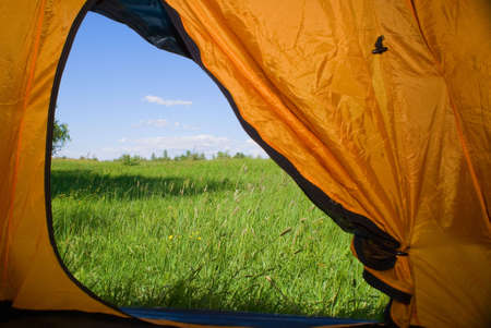 Kind from tent on lawn with green grass and blue skyの写真素材