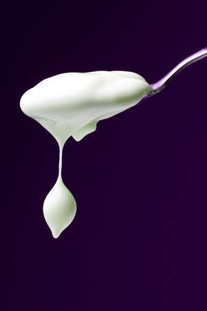 Spoon with yogurt on purple background