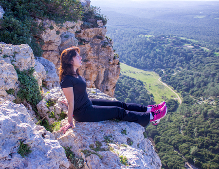 single woman in a black tracksuit sitting in the early morning on the cliff and looking into the distanceの写真素材