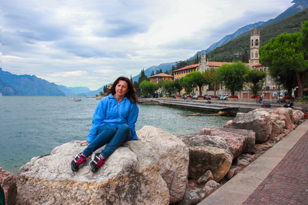 Woman sitting on a stone at the shores of Lake Garda, near Castelletto, Italyの写真素材
