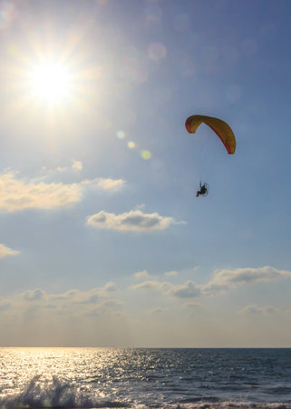 parachute jumper on motorized parachute flying over the sea at sunsetの写真素材