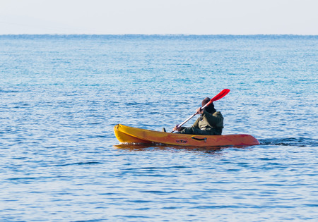 Nahariyya, Israel - February 04, 2017 : Fisherman in a green jumpsuit floats in orange kayak on the sea, near the coast of Nahariyya, Israel.のeditorial素材