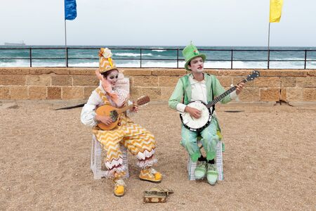 Caesarea, Israel, March 11, 2017 : Participants of the Purim festival dressed in costumes of clowns sitting on the waterfront and playing stringed instruments in Caesarea, Israelのeditorial素材