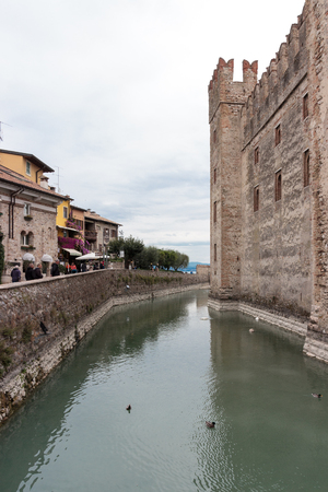 Sirmione, Italy - October 01, 2015 : Tourists walk along the embankment near the Castello Scaligero fortress wall in Sirmione, Italyのeditorial素材