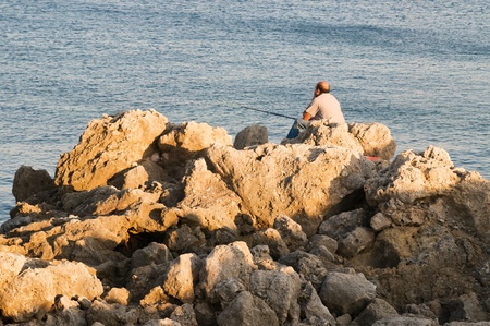 Bold fishmen is sitting on the rocks on sunsetの写真素材