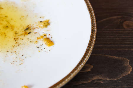 Food leftovers after meal. Yellow fat with spices on a single white plate. Wooden table background. Closeup shotの写真素材