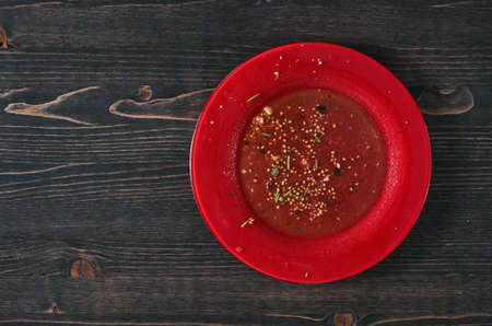 Salad leftovers after meal. Oil, tomato seeds, chopped parsley on a single red plate. Wooden table background. Top down flat photo with copy spaceの写真素材