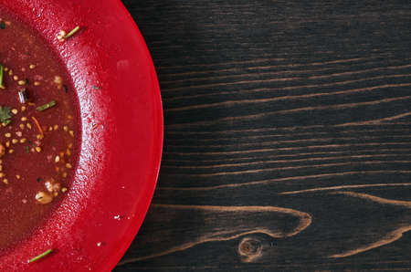 Salad leftovers after meal. Oil, tomato seeds, chopped parsley on a single red plate.  Wooden table background. Top down flat photo with copy space. Closeup shotの写真素材