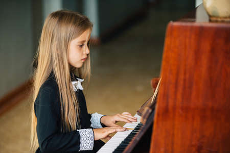 Little girl in a black dress learns to play the piano. The child plays a musical instrument.の写真素材
