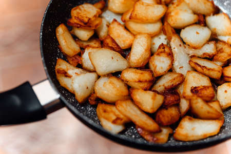 Fried pieces of potato in the pan. Harmful food close up.