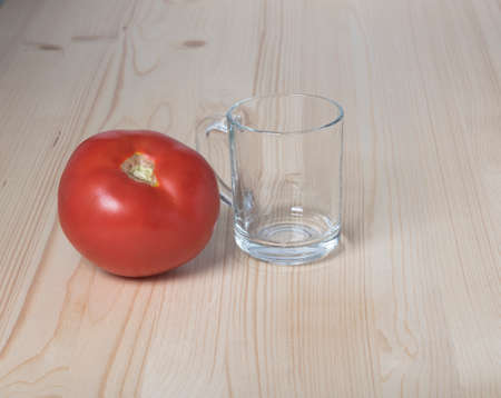 Red tomato and an empty glass mugの写真素材