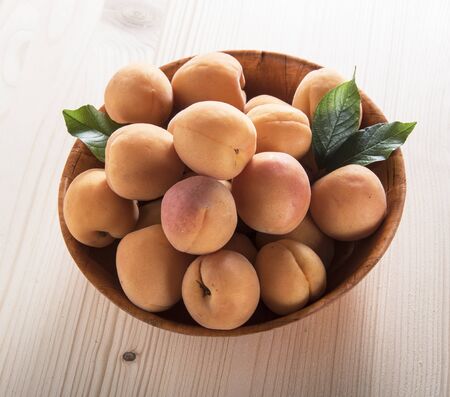 Ripe apricots with green leaves in the bowl on a wooden backgroundの写真素材