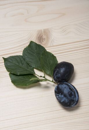 Two ripe plums with green leaves on a wooden backgroundの写真素材