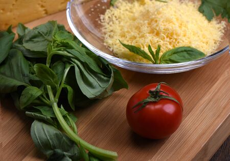 Tomato with basil, cheese in the backgroundon a cutting boardの写真素材