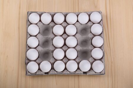 White chicken eggs in a cardboard package with empty spaces, wooden background. Looks like zero - zeroの写真素材