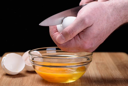 Destruction of a chicken white egg with a knife in male handsの写真素材