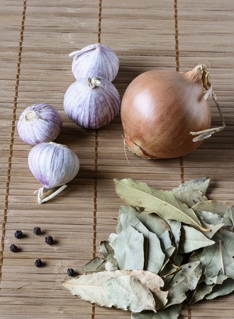 Dry bay leaf, onion and several garlic bulbs on a matの写真素材