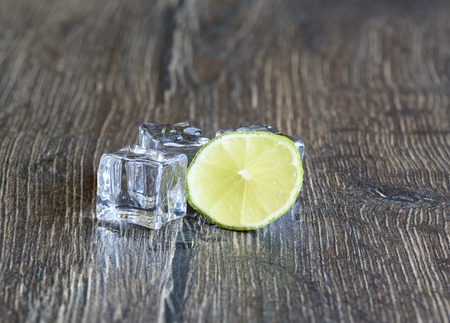 Cubes of ice and slice of lime in a wooden tableの写真素材
