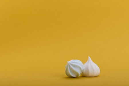 White and blue meringues isolated on yellow background with space for your textの写真素材