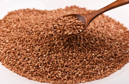 Wooden spoon full of buckwheat over a pile of buckwheat